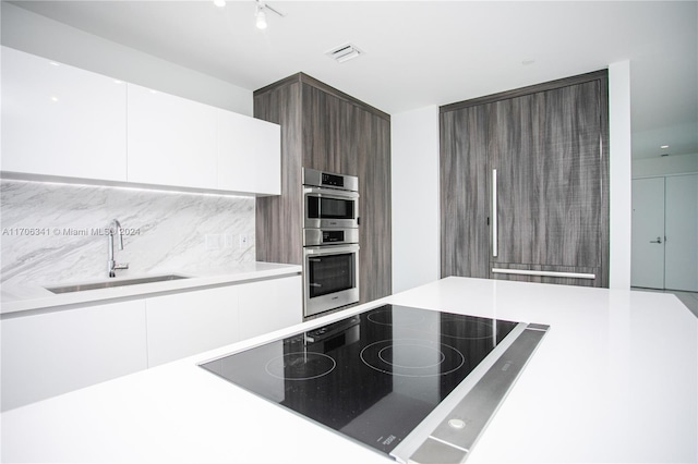 kitchen featuring backsplash, white cabinets, sink, black electric cooktop, and stainless steel double oven