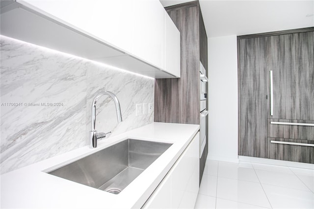 kitchen featuring tasteful backsplash, stainless steel oven, sink, light tile patterned floors, and white cabinetry