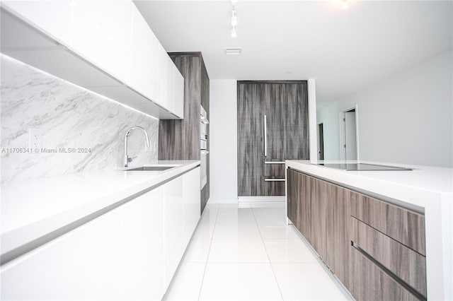 kitchen featuring backsplash, white cabinets, black electric stovetop, sink, and light tile patterned flooring