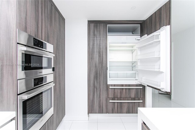 kitchen featuring dark brown cabinets, stainless steel double oven, and light tile patterned floors