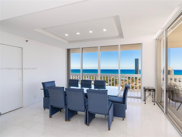 dining room with a water view, a raised ceiling, floor to ceiling windows, and light tile patterned flooring