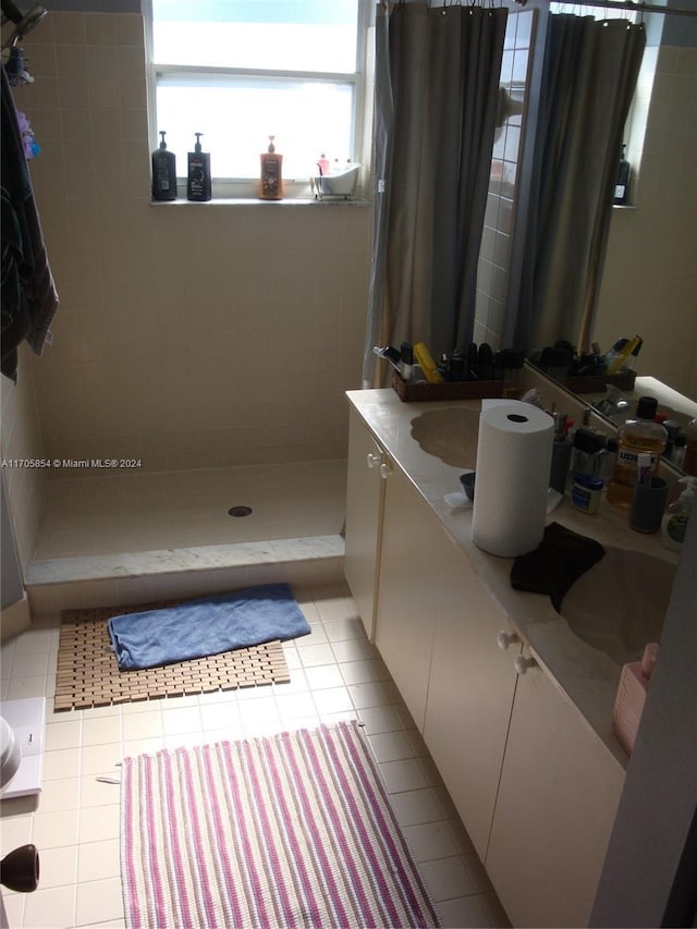 bathroom with tile patterned flooring, a tile shower, and vanity