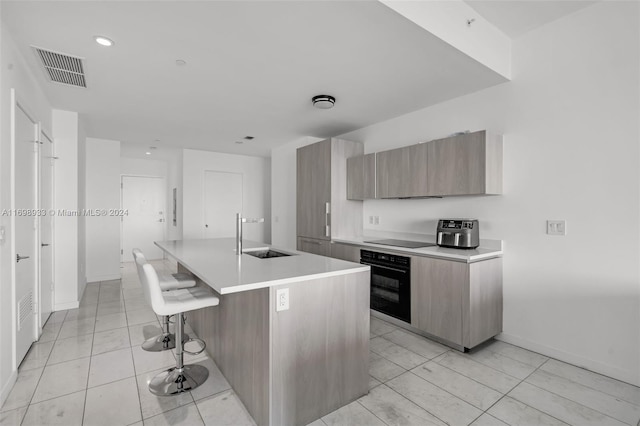 kitchen with a kitchen bar, sink, black appliances, light tile patterned floors, and a center island with sink