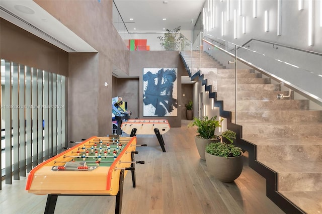 recreation room with hardwood / wood-style floors and a towering ceiling