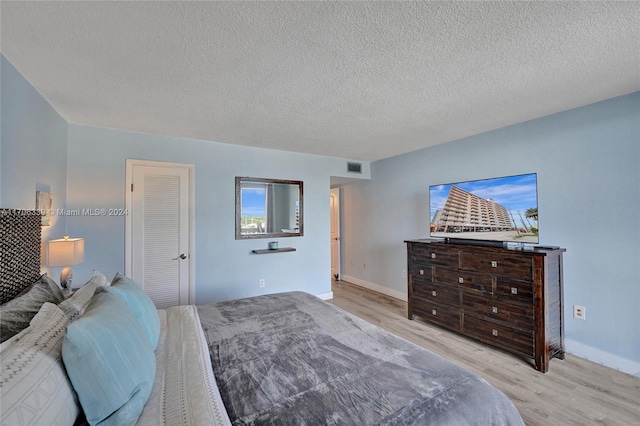 bedroom with a closet, a textured ceiling, and light hardwood / wood-style flooring