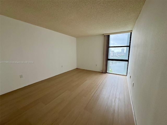 spare room with wood-type flooring, a textured ceiling, and a wall of windows