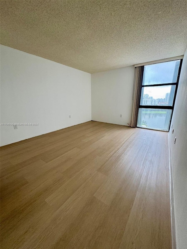 spare room featuring light wood-type flooring, a textured ceiling, and a wall of windows