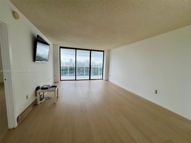 unfurnished room featuring light wood-type flooring, a textured ceiling, and a wall of windows