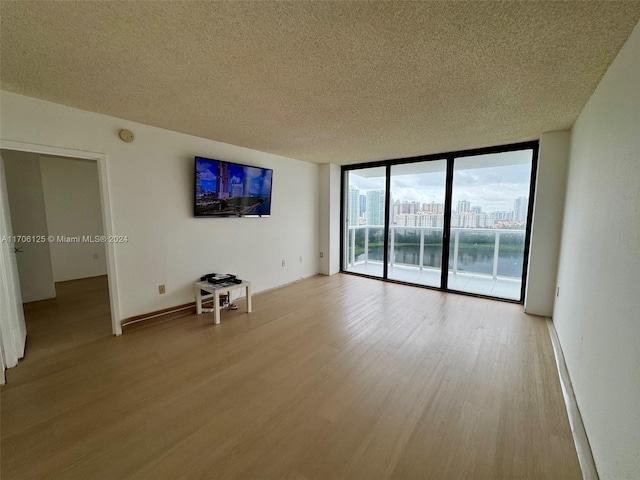 spare room with a wall of windows, a textured ceiling, and light wood-type flooring