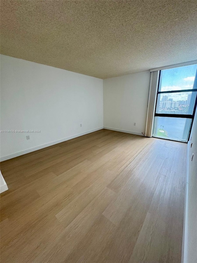 unfurnished room featuring a textured ceiling, light wood-type flooring, and a wall of windows