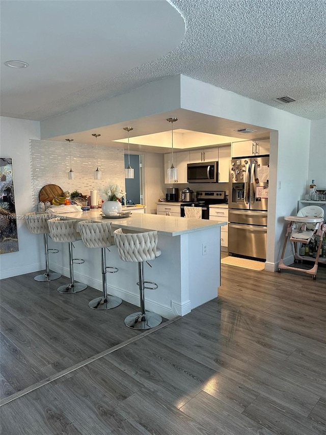 kitchen featuring kitchen peninsula, appliances with stainless steel finishes, a kitchen breakfast bar, decorative light fixtures, and white cabinetry