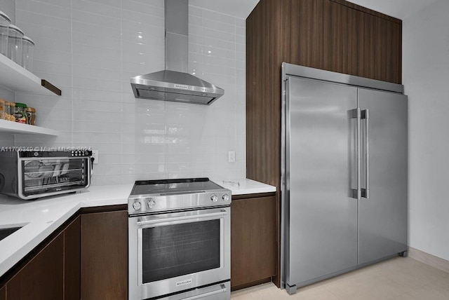 kitchen featuring dark brown cabinets, decorative backsplash, wall chimney range hood, and appliances with stainless steel finishes