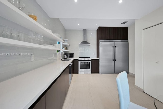 kitchen with sink, wall chimney exhaust hood, tasteful backsplash, dark brown cabinets, and appliances with stainless steel finishes