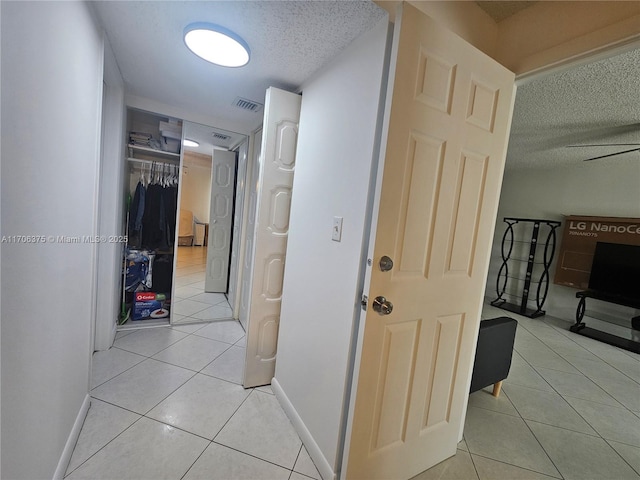 hall featuring light tile patterned floors, baseboards, visible vents, and a textured ceiling