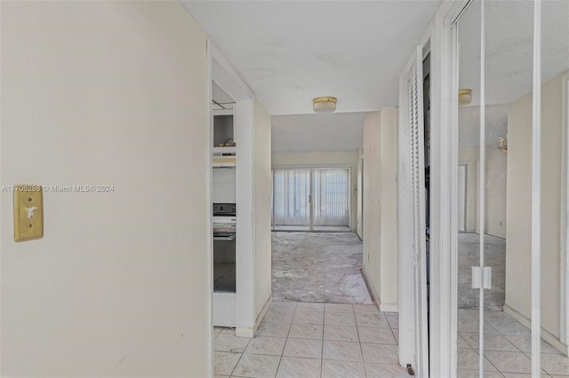 corridor with a textured ceiling and light tile patterned flooring