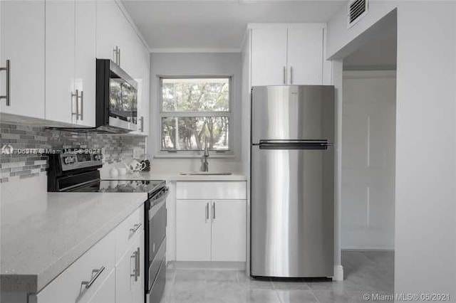 kitchen featuring stainless steel appliances, light stone countertops, decorative backsplash, white cabinets, and sink