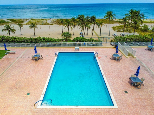 community pool with a water view, a patio area, and fence