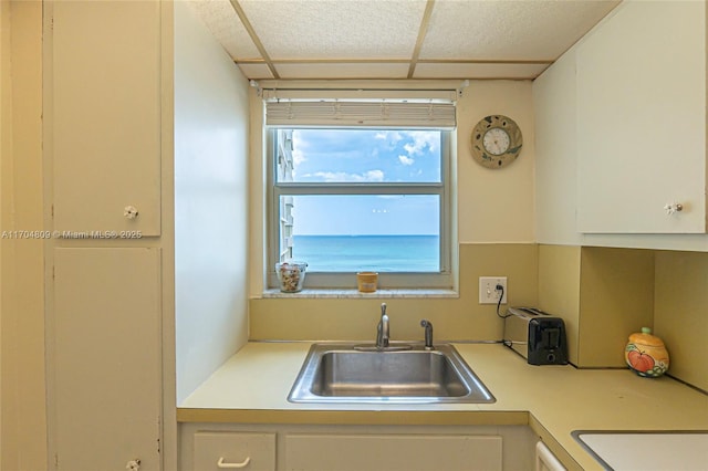 kitchen with sink, a drop ceiling, and white cabinets