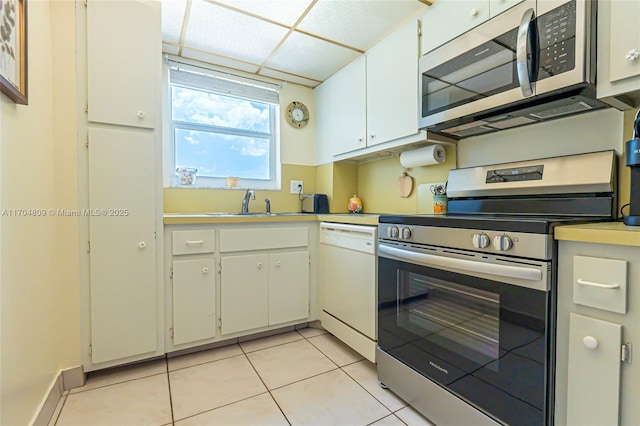 kitchen with appliances with stainless steel finishes, sink, light tile patterned floors, and white cabinets