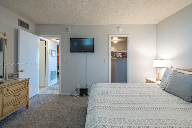 bedroom with a walk in closet, light carpet, a closet, and a textured ceiling