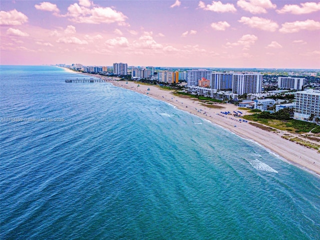 aerial view at dusk featuring a view of the beach and a water view