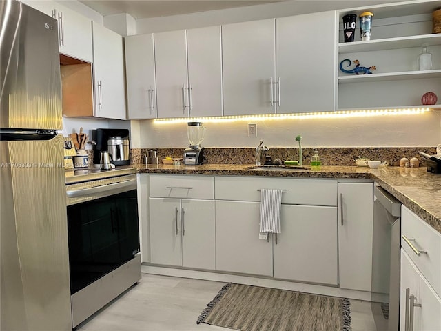 kitchen with dark stone counters, sink, light wood-type flooring, appliances with stainless steel finishes, and white cabinetry