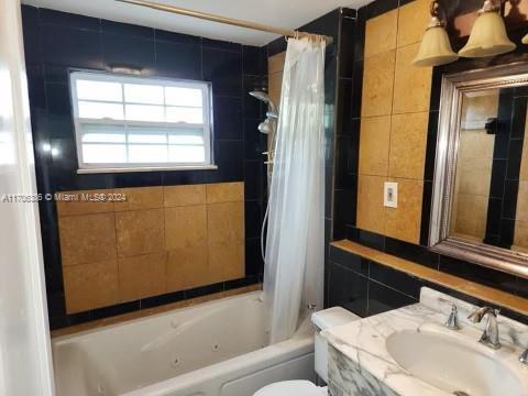 full bathroom with vanity, toilet, shower / bathtub combination with curtain, and tile walls