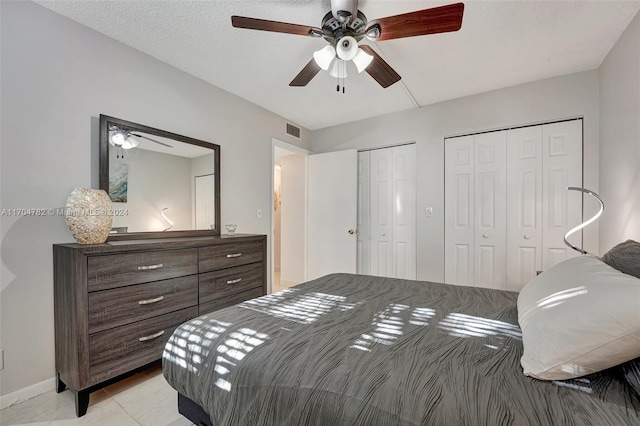 bedroom with a textured ceiling, ceiling fan, light tile patterned floors, and two closets