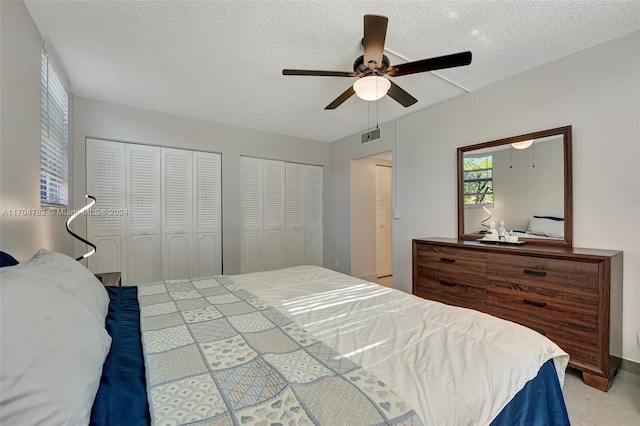 bedroom featuring two closets, ceiling fan, light carpet, and a textured ceiling