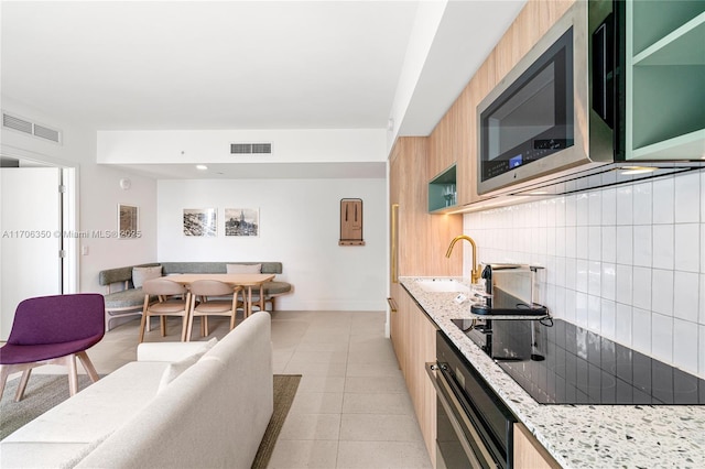 kitchen with backsplash, sink, light stone countertops, black oven, and light tile patterned flooring