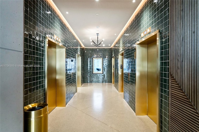 hallway featuring a chandelier, elevator, tile walls, and crown molding