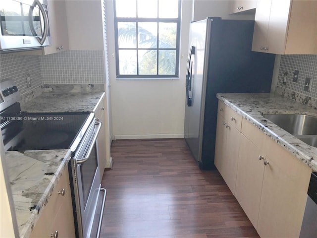 kitchen with dark wood-type flooring, light stone counters, cream cabinets, decorative backsplash, and appliances with stainless steel finishes