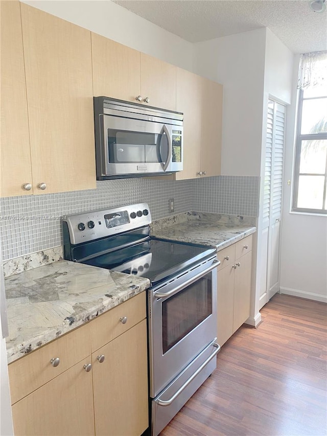 kitchen featuring light brown cabinets, wood-type flooring, backsplash, and appliances with stainless steel finishes