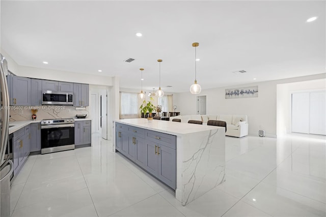 kitchen with gray cabinetry, stainless steel appliances, light stone counters, pendant lighting, and decorative backsplash