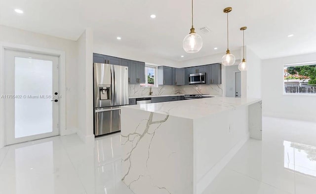 kitchen featuring pendant lighting, backsplash, appliances with stainless steel finishes, light stone counters, and kitchen peninsula