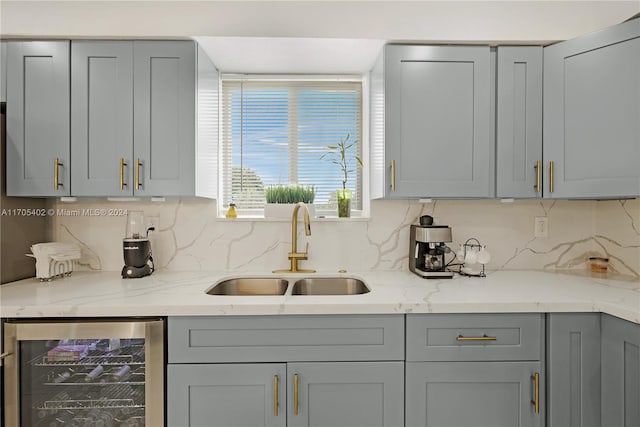 kitchen with light stone counters, gray cabinets, wine cooler, and sink