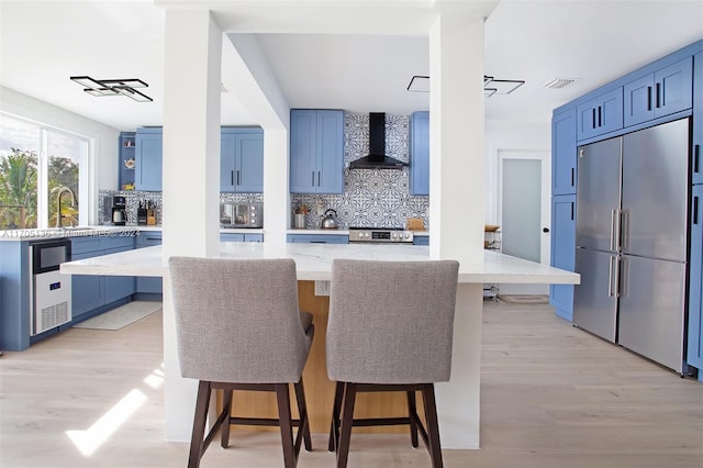 kitchen with a breakfast bar, light wood-type flooring, wall chimney range hood, and stainless steel appliances