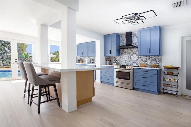 kitchen with wall chimney exhaust hood, a kitchen breakfast bar, tasteful backsplash, stainless steel electric range, and light wood-type flooring