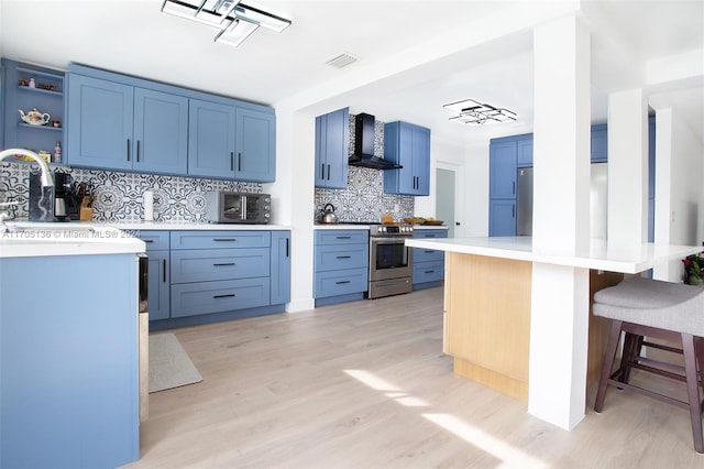 kitchen featuring appliances with stainless steel finishes, tasteful backsplash, a breakfast bar, wall chimney range hood, and light hardwood / wood-style floors