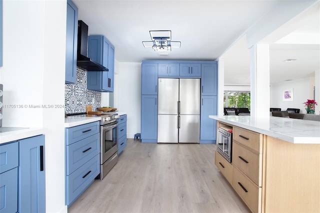 kitchen featuring backsplash, blue cabinets, wall chimney exhaust hood, light wood-type flooring, and stainless steel appliances