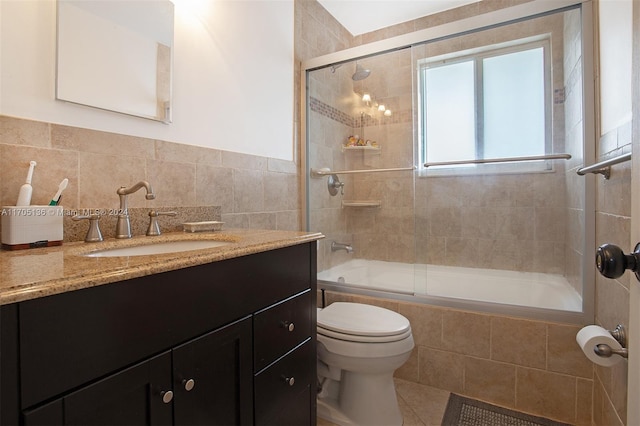 full bathroom featuring tile patterned flooring, toilet, shower / bath combination with glass door, vanity, and tile walls