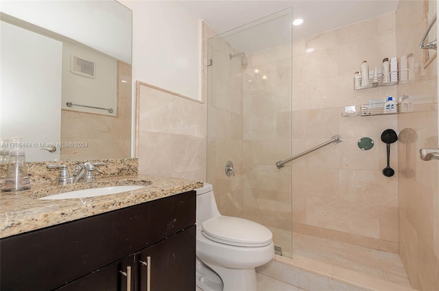 bathroom with vanity, toilet, tiled shower, and tile walls