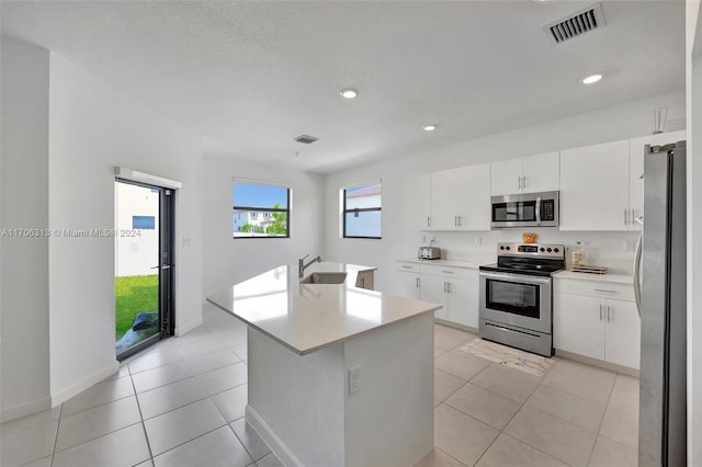 kitchen with a center island with sink, sink, light tile patterned floors, appliances with stainless steel finishes, and white cabinetry