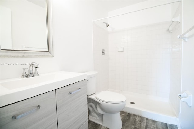 bathroom featuring tiled shower, vanity, hardwood / wood-style flooring, and toilet