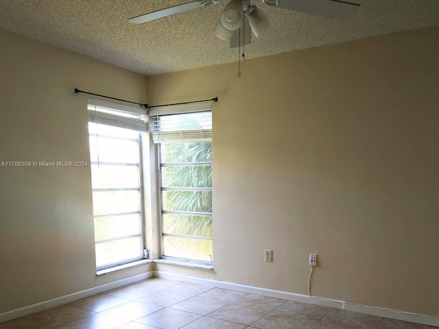 empty room with ceiling fan, a healthy amount of sunlight, light tile patterned flooring, and a textured ceiling