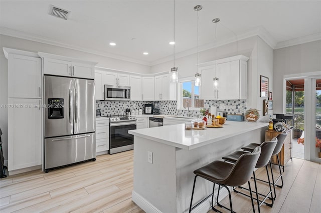 kitchen featuring a breakfast bar, white cabinets, decorative light fixtures, kitchen peninsula, and stainless steel appliances