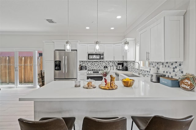 kitchen with pendant lighting, sink, a kitchen bar, white cabinetry, and stainless steel appliances