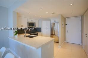 kitchen with kitchen peninsula, stainless steel appliances, sink, light tile patterned floors, and white cabinetry