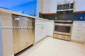 kitchen featuring decorative backsplash, appliances with stainless steel finishes, white cabinetry, and light tile patterned flooring