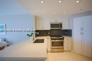 kitchen with white cabinetry, sink, decorative backsplash, light tile patterned floors, and appliances with stainless steel finishes